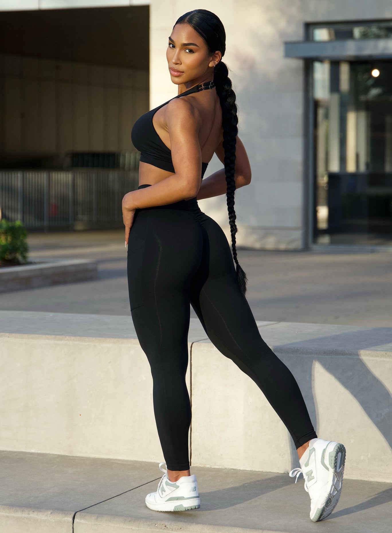 Left side profile view of a model facing to her left wearing our black V scrunch back leggings along with the matching bra 