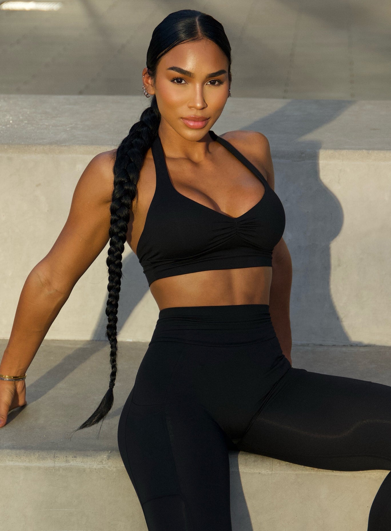 Front profile view of a model sitting on a step wearing our black backless bra along with the v back leggings 