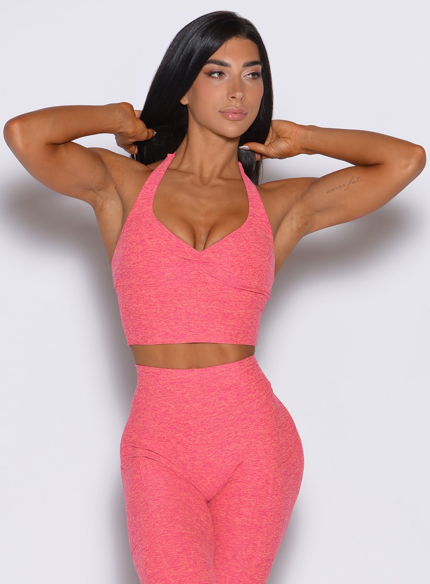 front profile view of a model adjusting her hair wearing our longline backless bra in Neon Tangerine Shock color along with a matching leggings