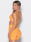 left side profile view of a model looking over her shoulder wearing the Voltage sports bra in Kumquat color