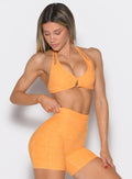 front profile view of a model with one hand on the waistband of the shorts wearing the Voltage sports bra in Kumquat color