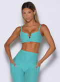 front profile view of a model with both hands inside the side pockets of the leggings wearing the Wave wire bra in crystal current color