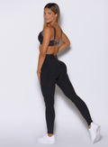 left side profile view of a model looking over her shoulder wearing the Wave Wire Leggings in Heathered Black color