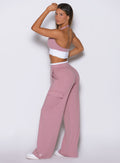 Back left side view of model wearing Bombshell Sportswear wide leg joggers in Cosmetic Pink color, posing with one hand raised and relaxed flowy fit