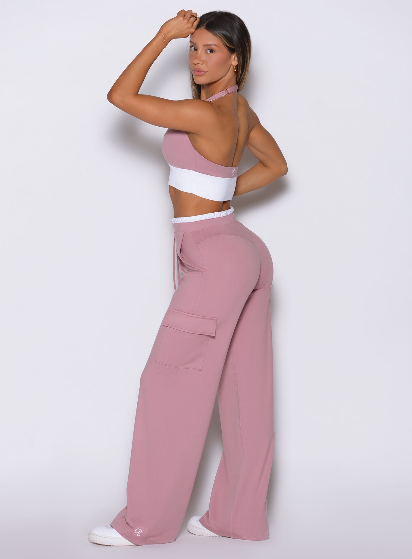 Back left side view of model wearing Bombshell Sportswear wide leg joggers in Cosmetic Pink color, posing with one hand raised and relaxed flowy fit