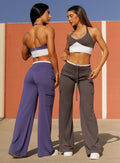 Front and back view of two models in outdoors wearing Bombshell Sportswear Confidence bra tops in Future Dusk and Champion Grey colors paired with matching wide leg joggers, featuring sculpting supportive fit and coordinated sets