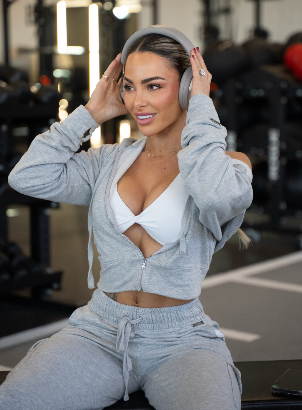 Woman in gray athletic wear sitting on a bench in a gym.