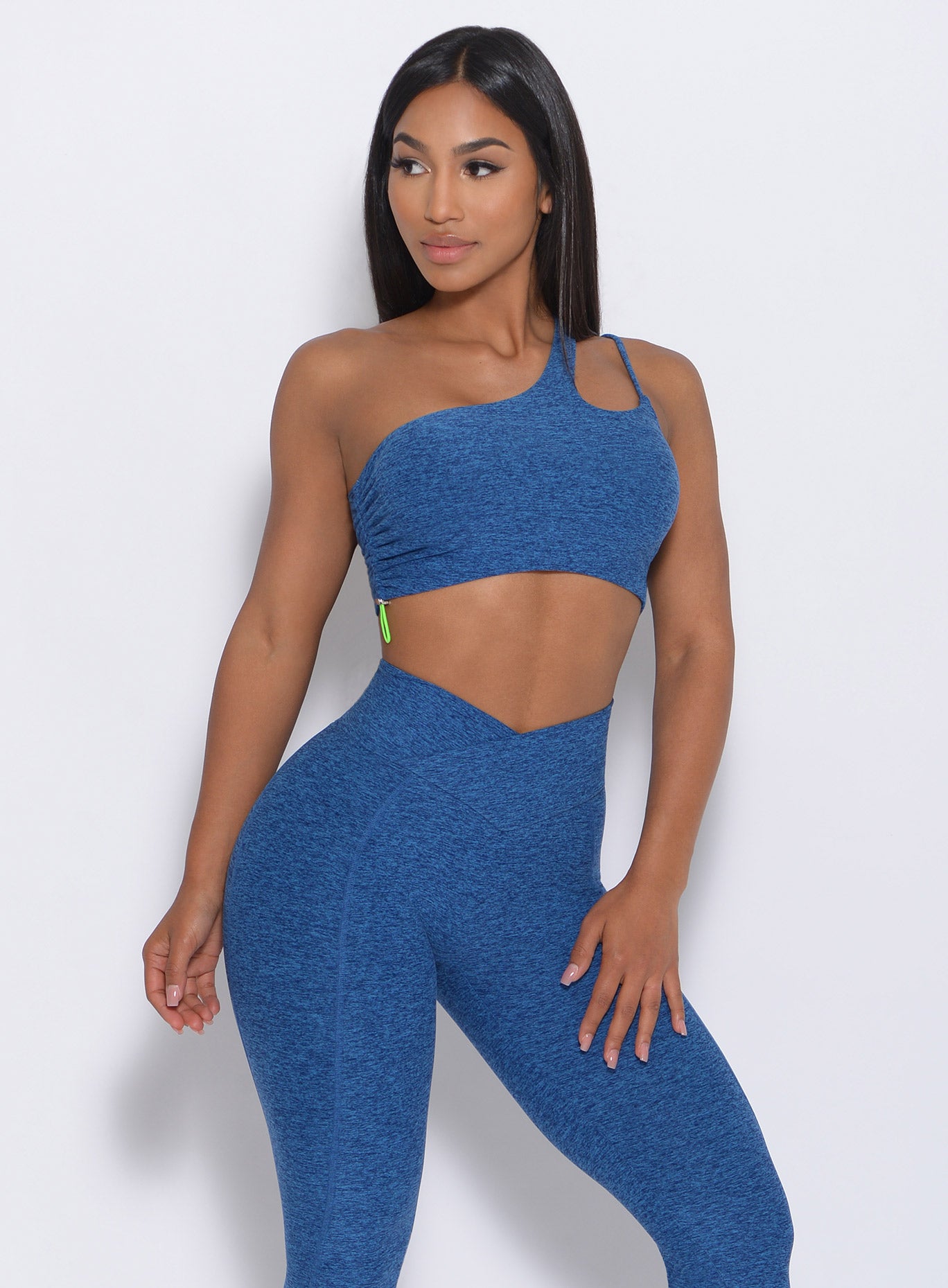 Zoomed in front profile of the model with her left hand on thigh wearing our asymmetrical scrunch bra in ocean color and a matching leggings