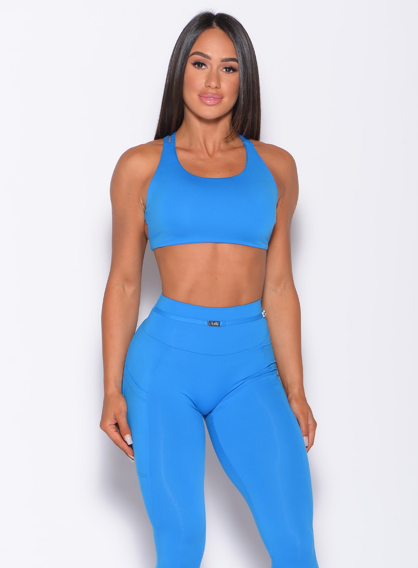 Front profile view of a model in our barbell sports bra in crystal pop blue color and a matching leggings