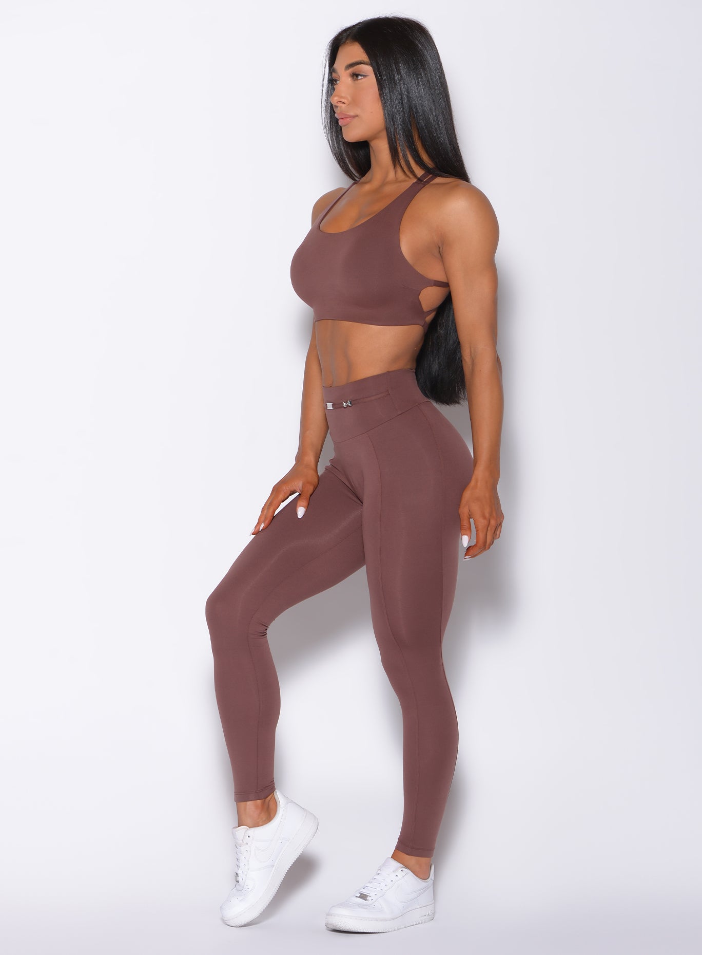 Left side profile view of a model angled left wearing our barbell leggings in chocolate color and a matching bra
