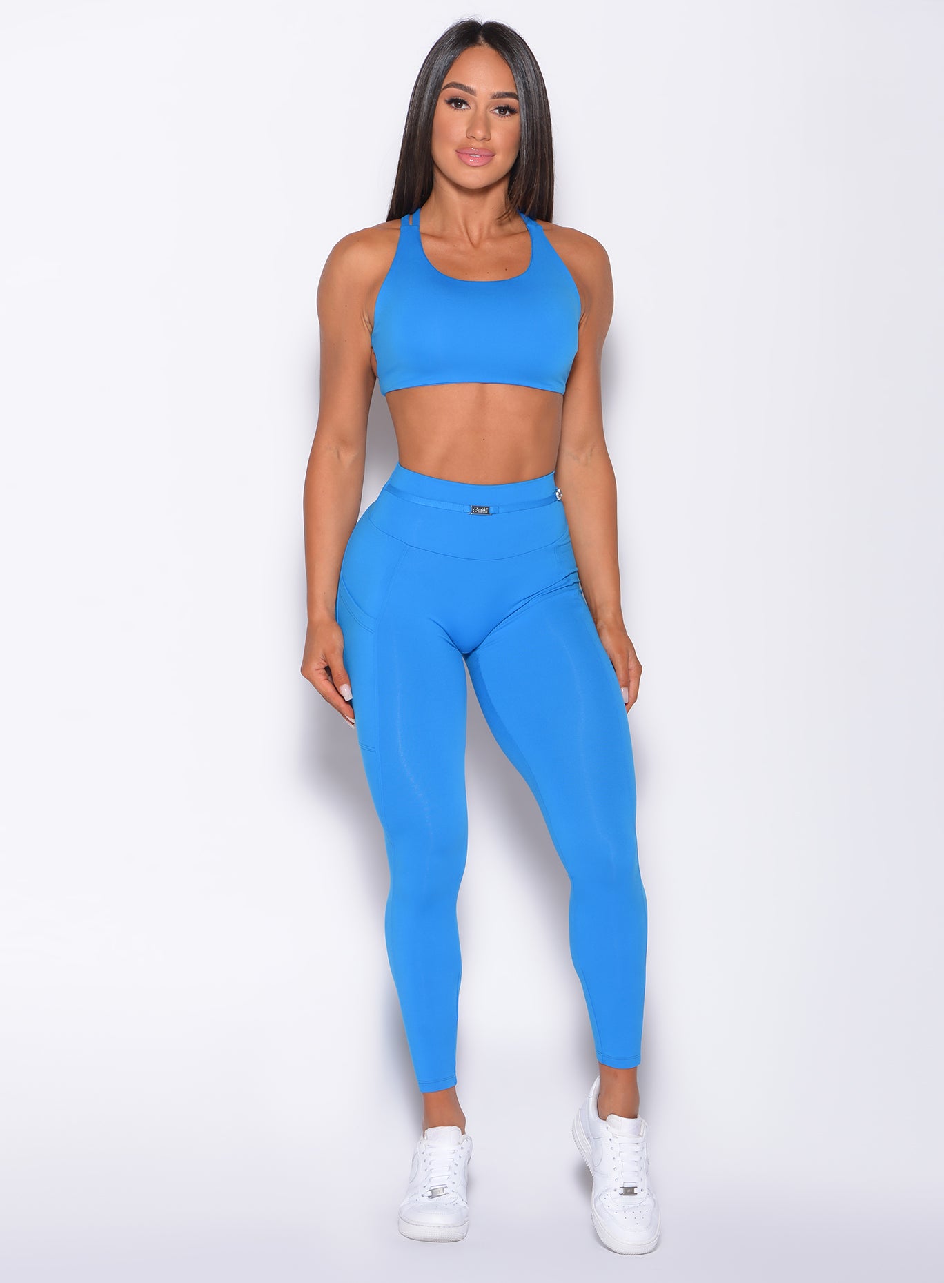 front profile view of a model facing forward wearing our barbell leggings in crystal pop blue color and a matching bra