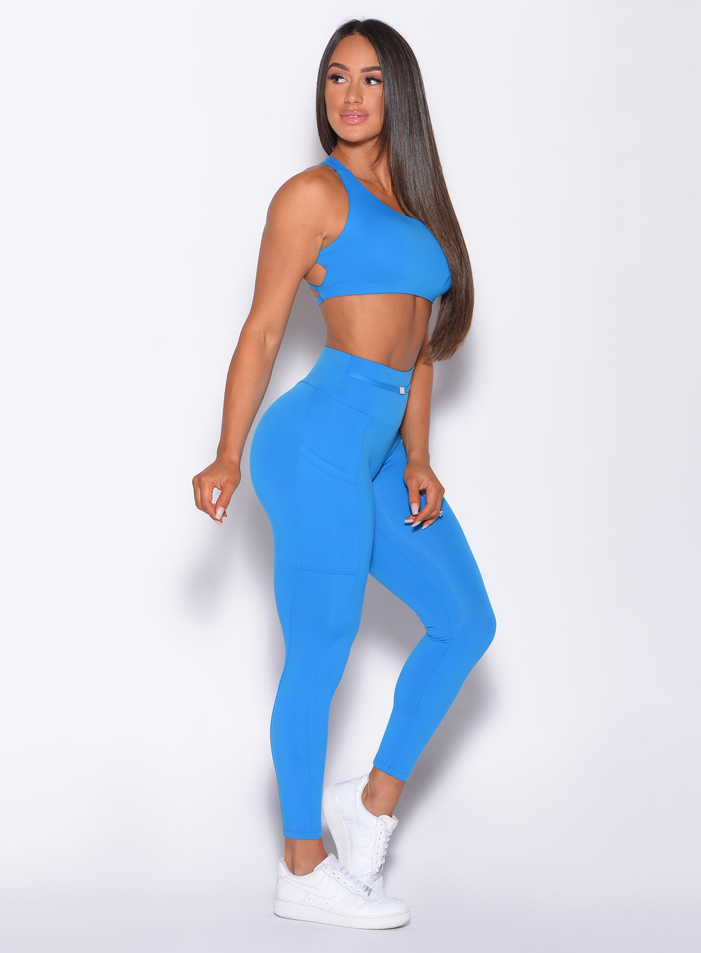 Right side profile view of a model in our barbell leggings in crystal pop blue color and a matching bra