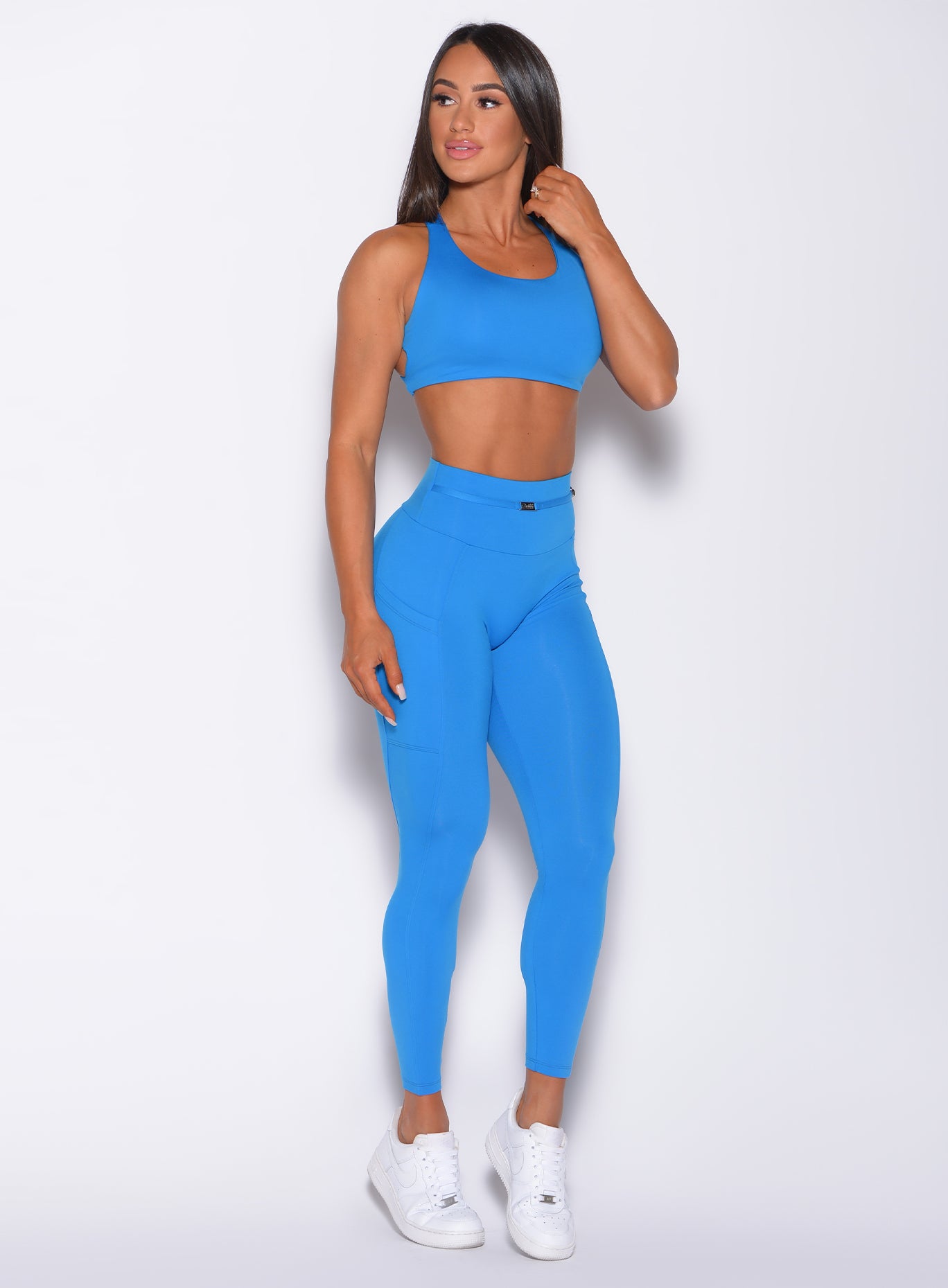Front profile view of a model wearing our barbell leggings in crystal pop blue color and a matching bra