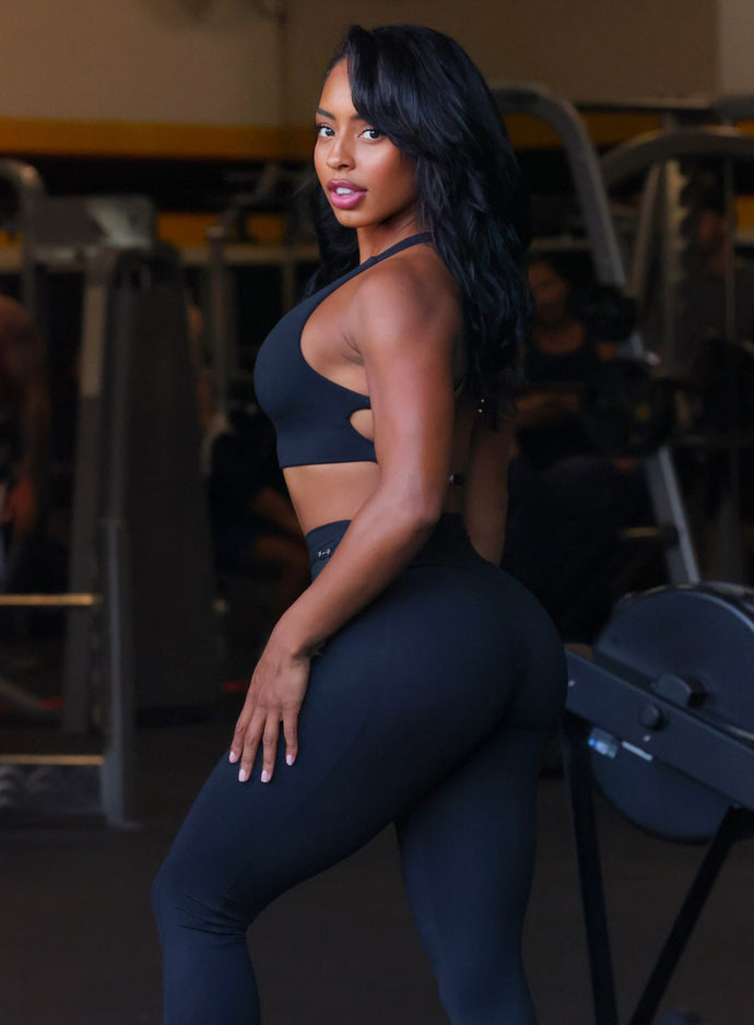 Left side profile view of a model facing to her left wearing our barbell sports bra in black and a matching leggings
