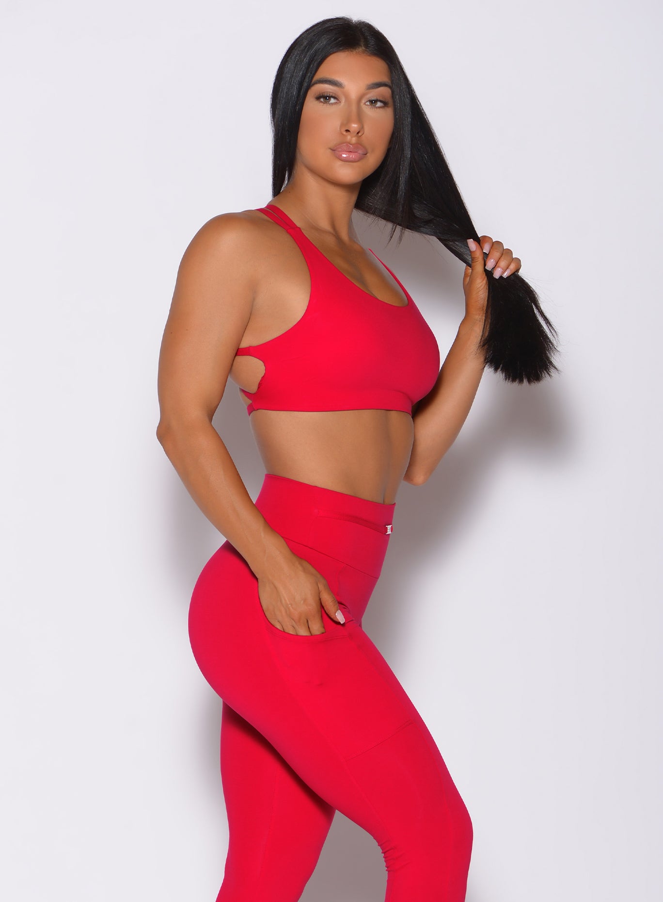 Right side profile view of a model angled right and holding her hair wearing our red barbell sports bra and a matching leggings