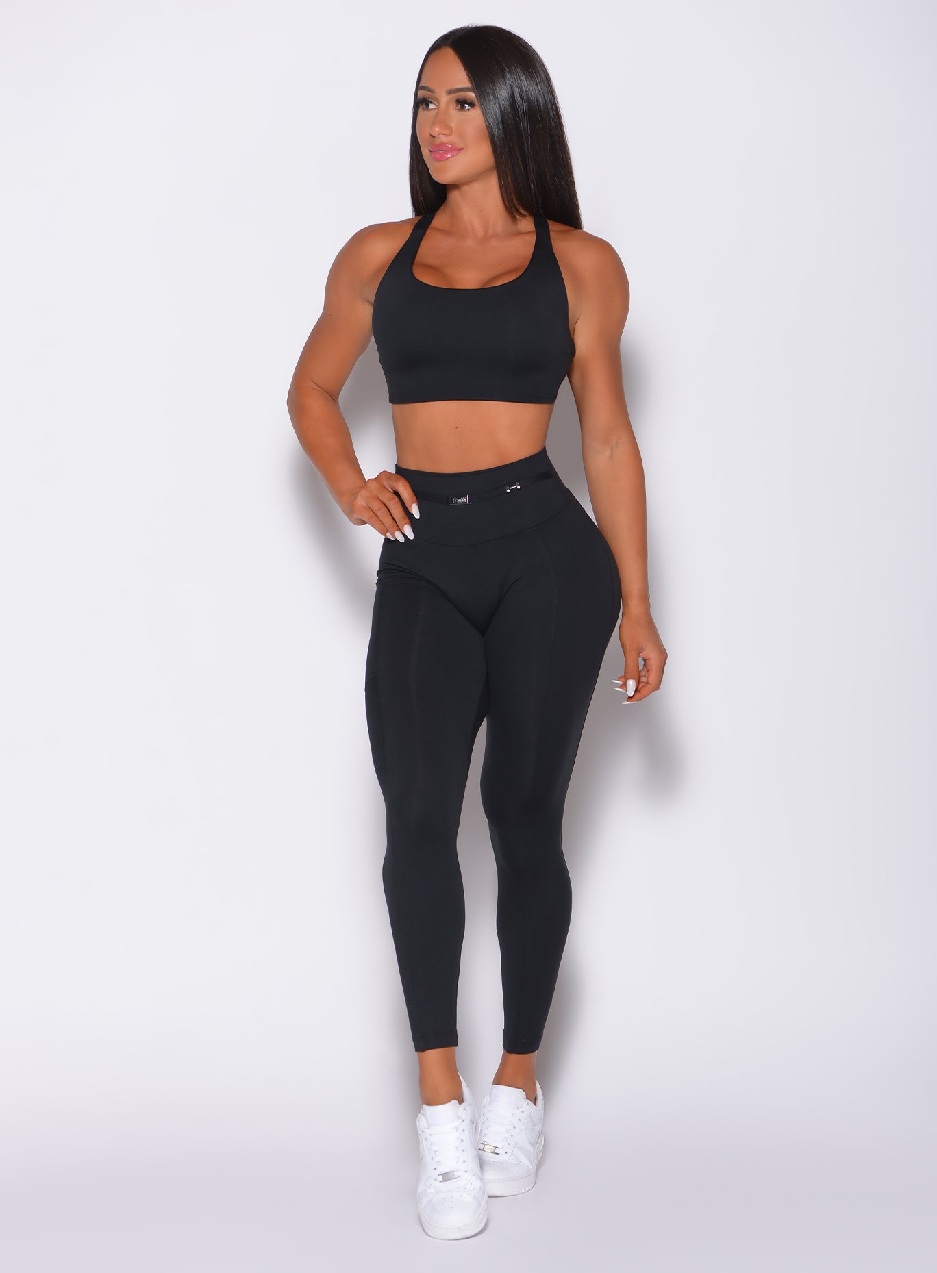 Front profile view of a model with her right hand on waist wearing our black barbell leggings  and a matching bra 