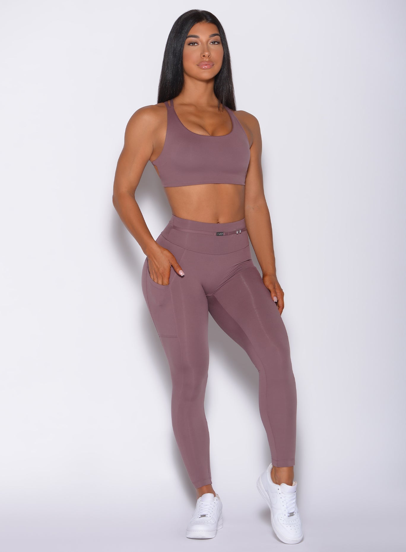 Front profile view of a model  with her left hand in pocket wearing our barbell legging in mauve color and a matching bra