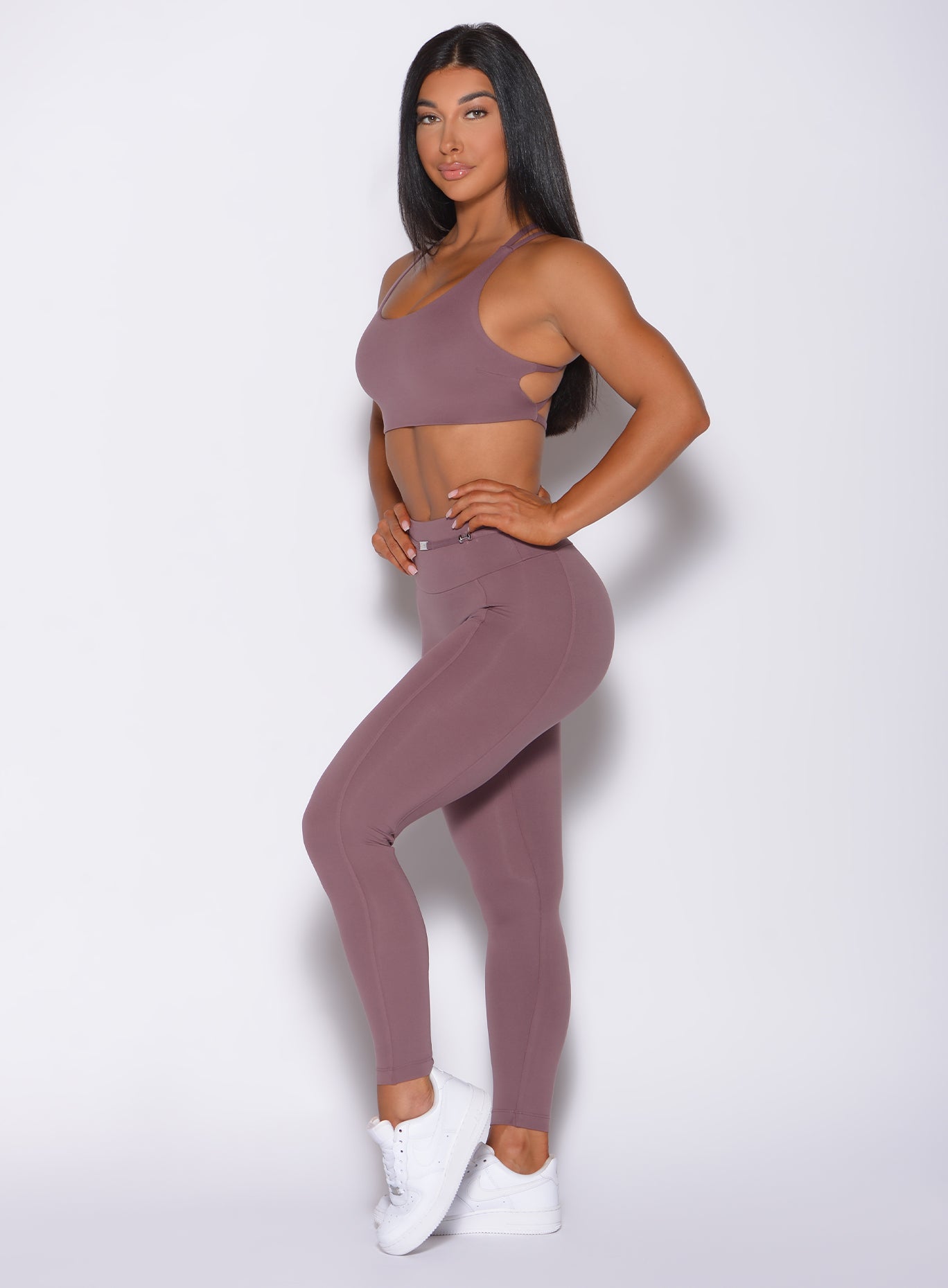 Left side profile view of a model with her hands on waist wearing  our barbell legging in mauve color and a matching bra