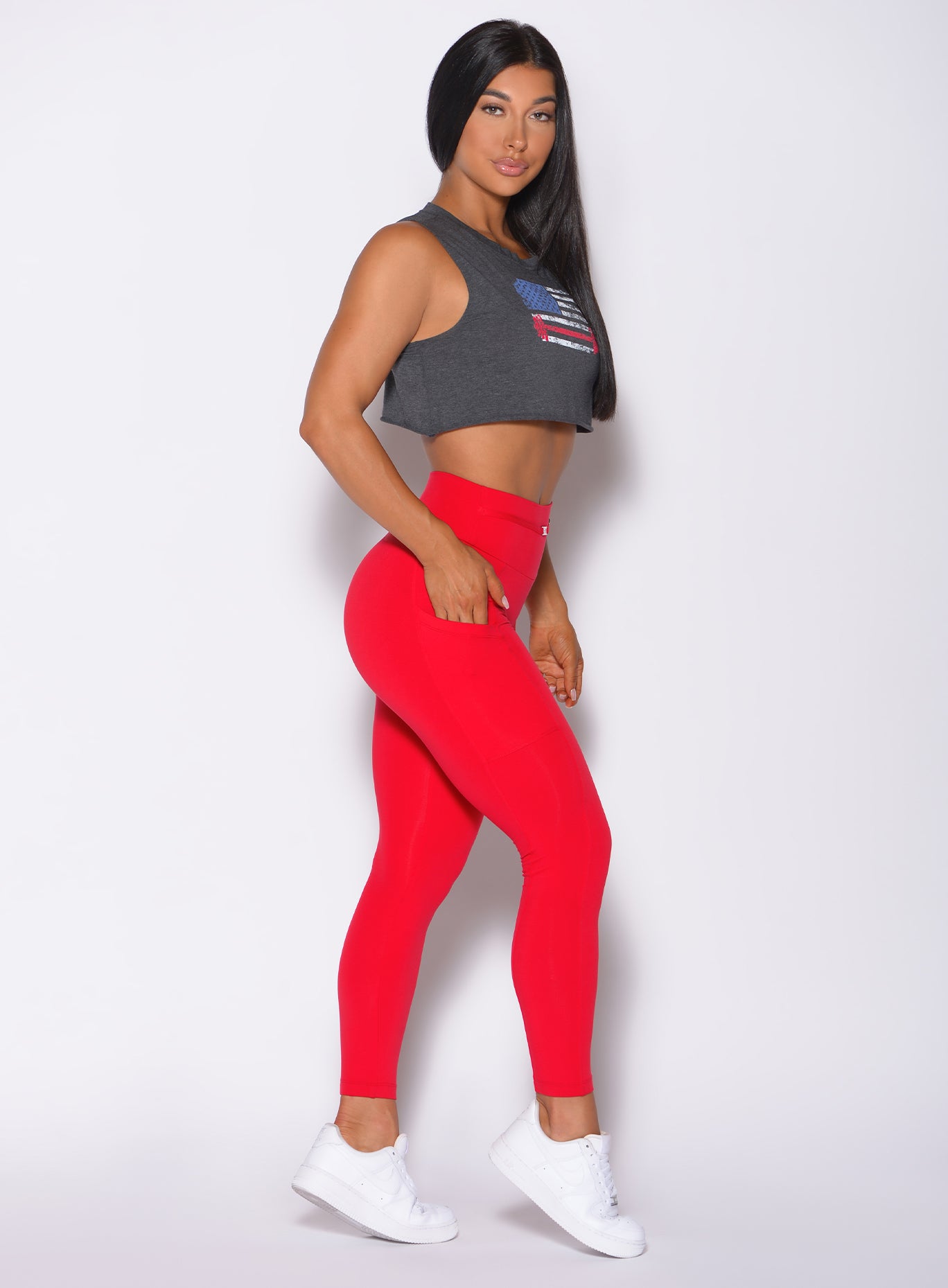 Right side profile view of a model facing to her right wearing our USA barbell tank in charcoal color and a red leggings