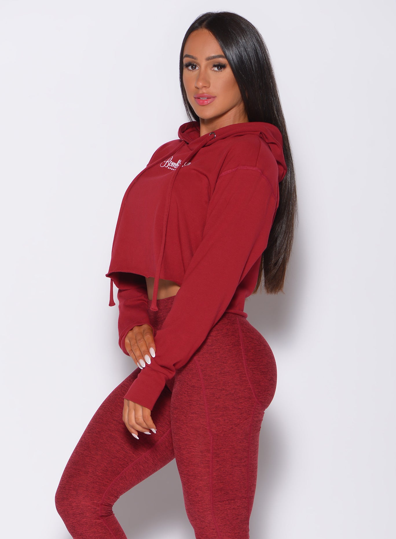 Left side profile view of a model angled left wearing our bombshell hoodie in red rose color and a matching leggings