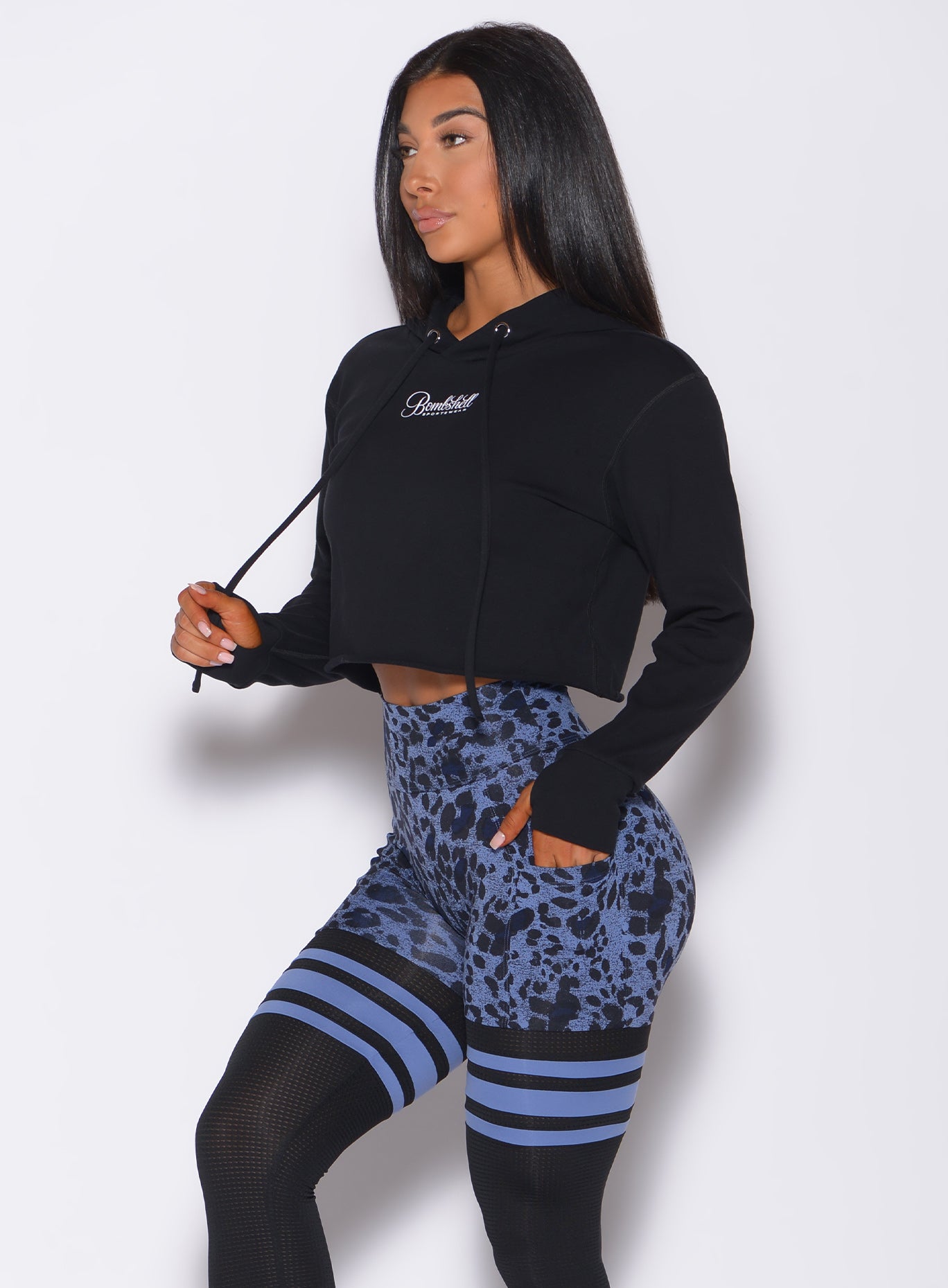 Left side  profile view of a model angled left wearing  our black bombshell hoodie and a cheetah print leggings