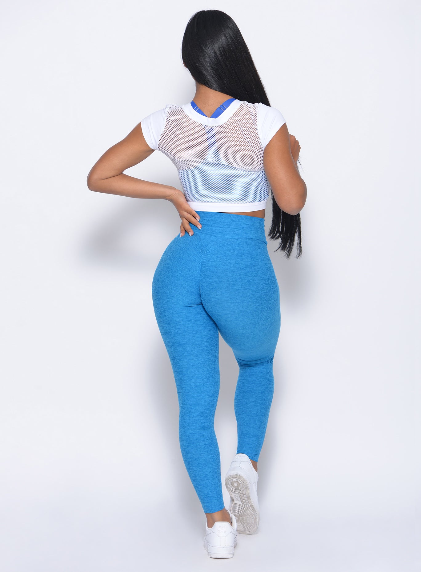 Back profile view of the model  with her left had on waist in our white mesh tee and a high waist leggings