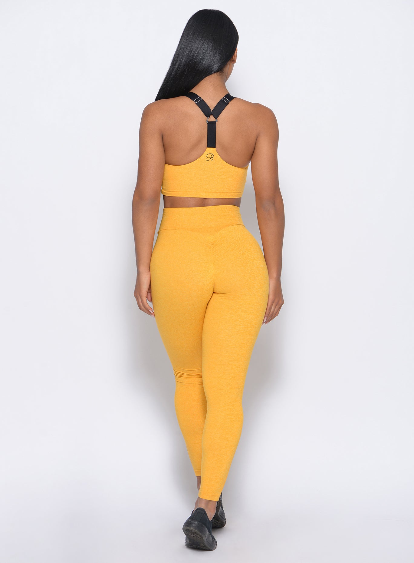 Back profile view of the model wearing our boost leggings in sunkissed color and a matching bra