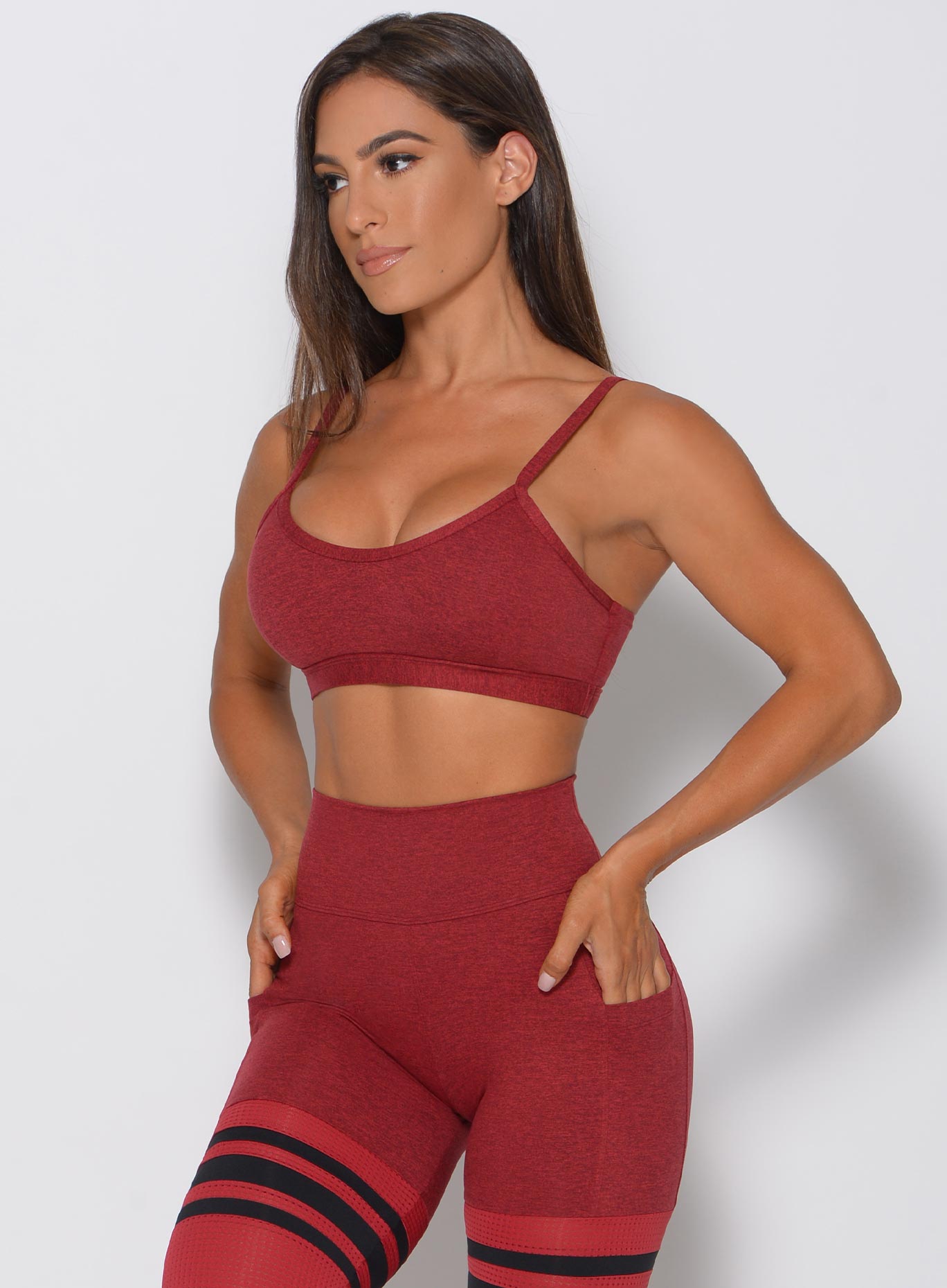 Model facing forward looking left wearing maroon sports bra and matching high waist leggings with hands in her pocket