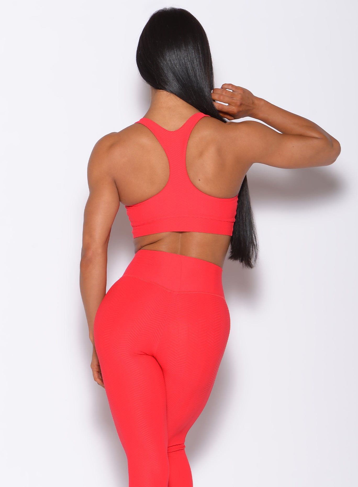 Front profile view of a model with her hands on waist wearing our chevron sports bra in flame red color and a matching leggings