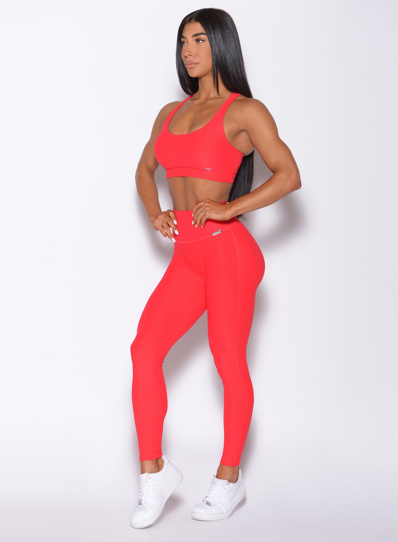 Left side profile view of a model angled left wearing our Chevron Leggings in flame red color and matching bra