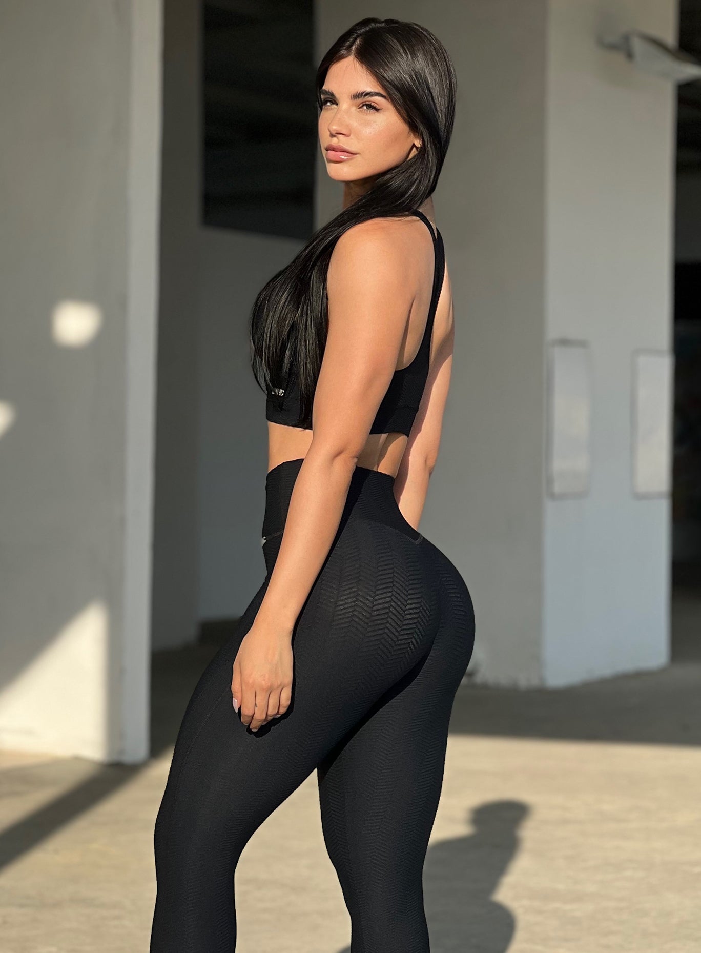 Left side profile view of a model wearing our chevron sports bra in jet black color and a matching leggings