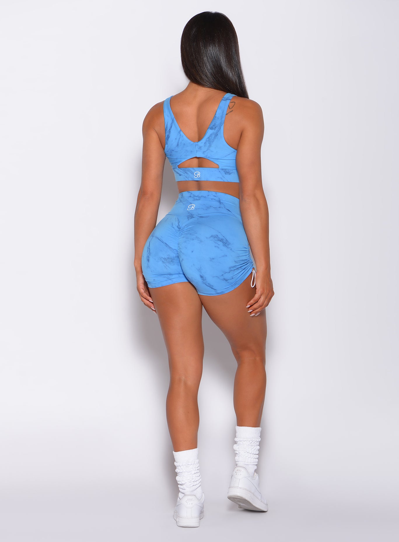 Back profile view of a model in our contour toggle shorts in marble blue color and a matching bra 
