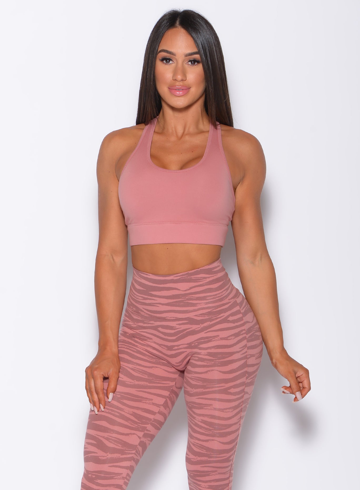 Front profile view of a model wearing our rival sports bra in solid blush color and a matching tiger print leggings