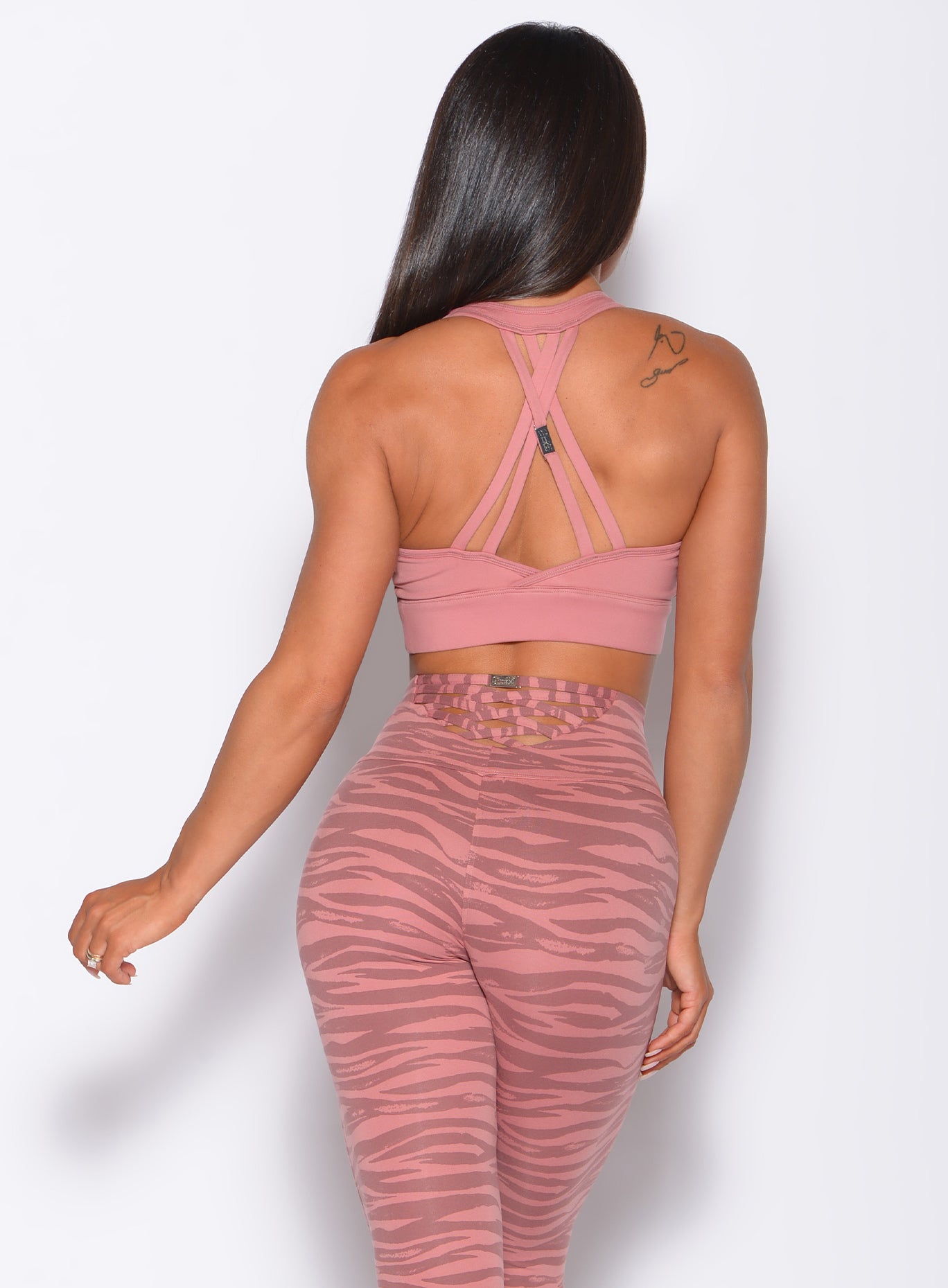 Back profile view of a model in our rival sports bra in solid blush color and a matching tiger print leggings