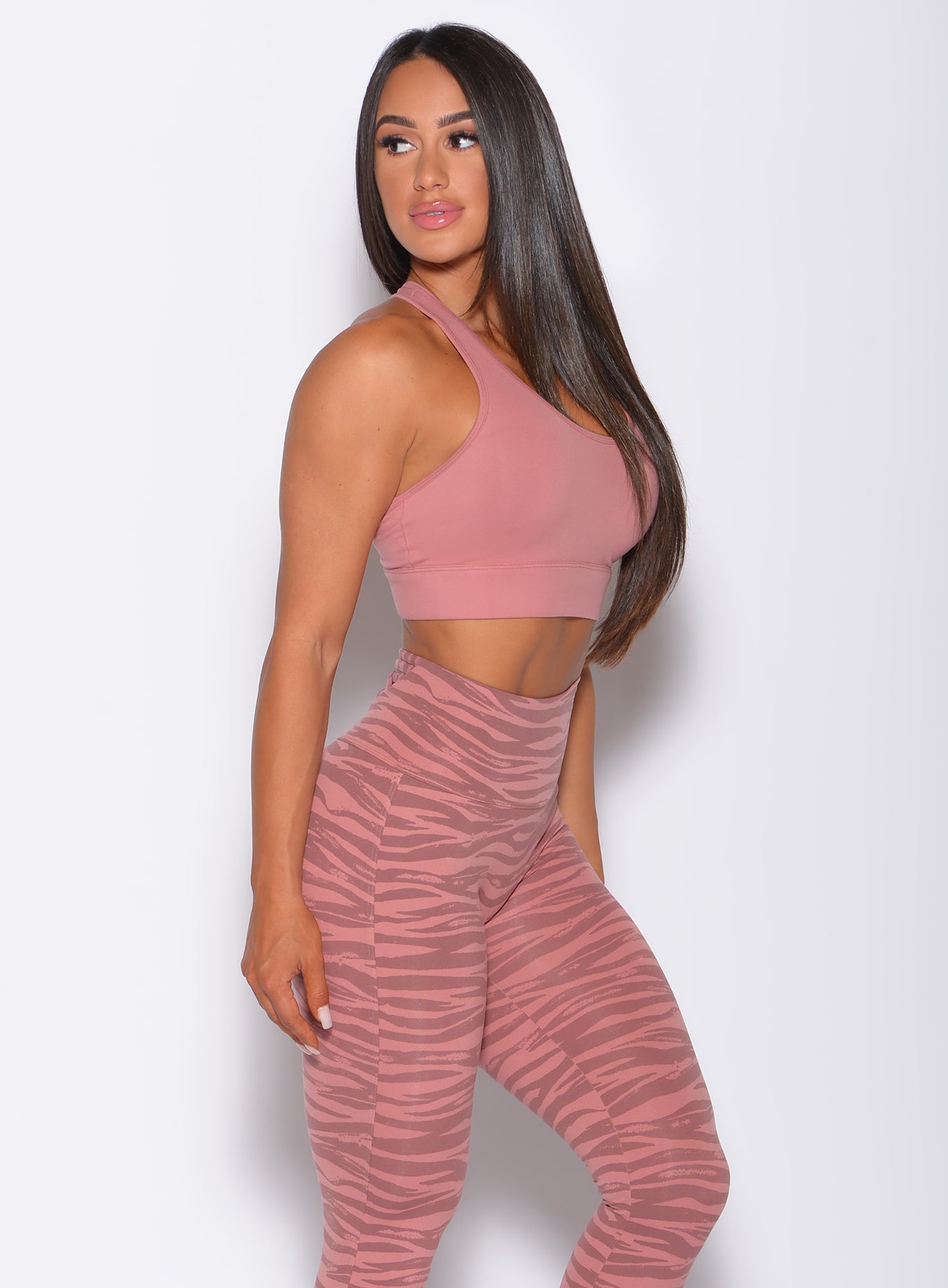 Right side profile view of a model in our rival sports bra in solid blush color and a matching tiger print leggings