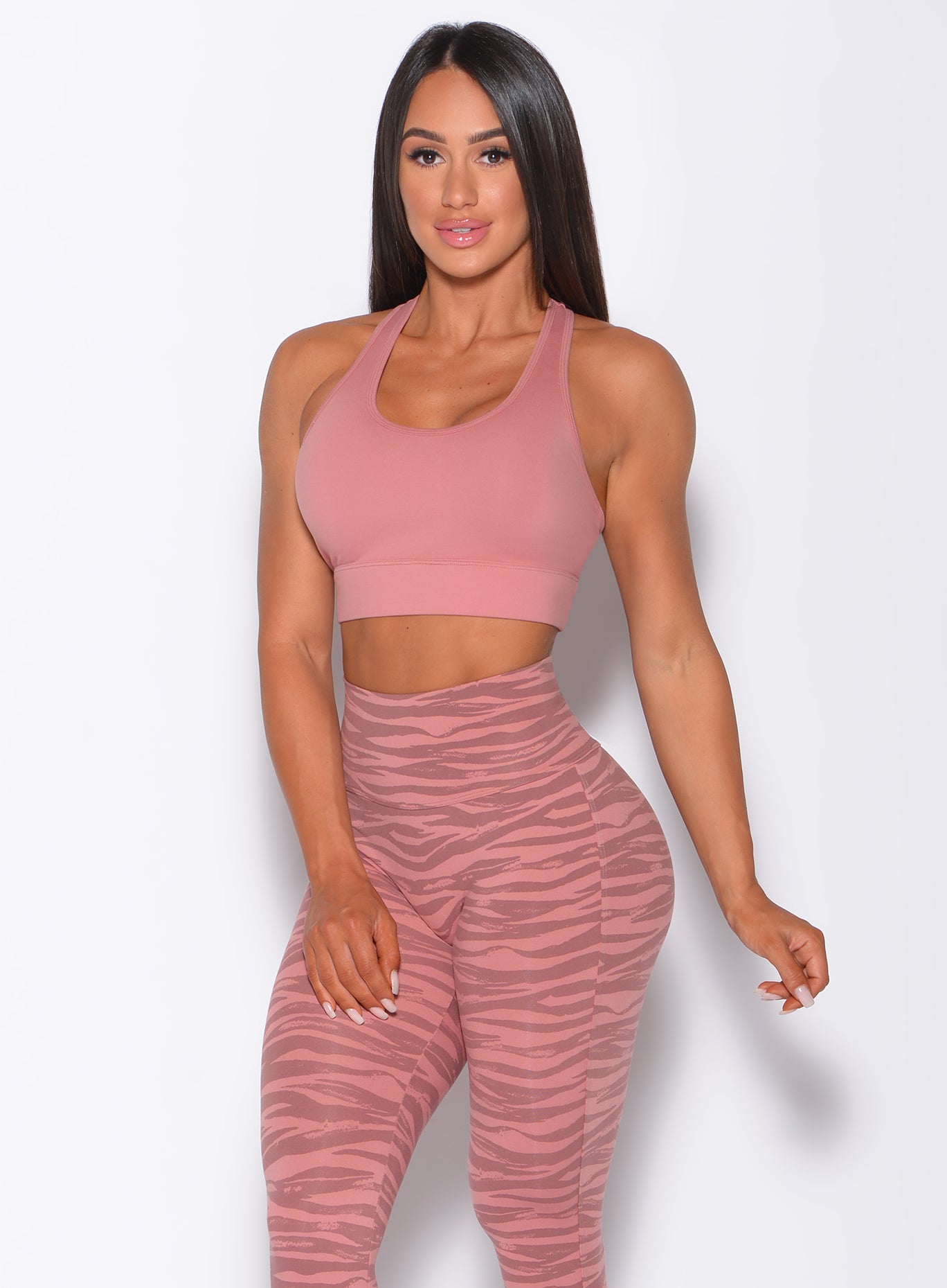 Front profile view of a model in our rival sports bra in solid blush color and a matching tiger print leggings 
