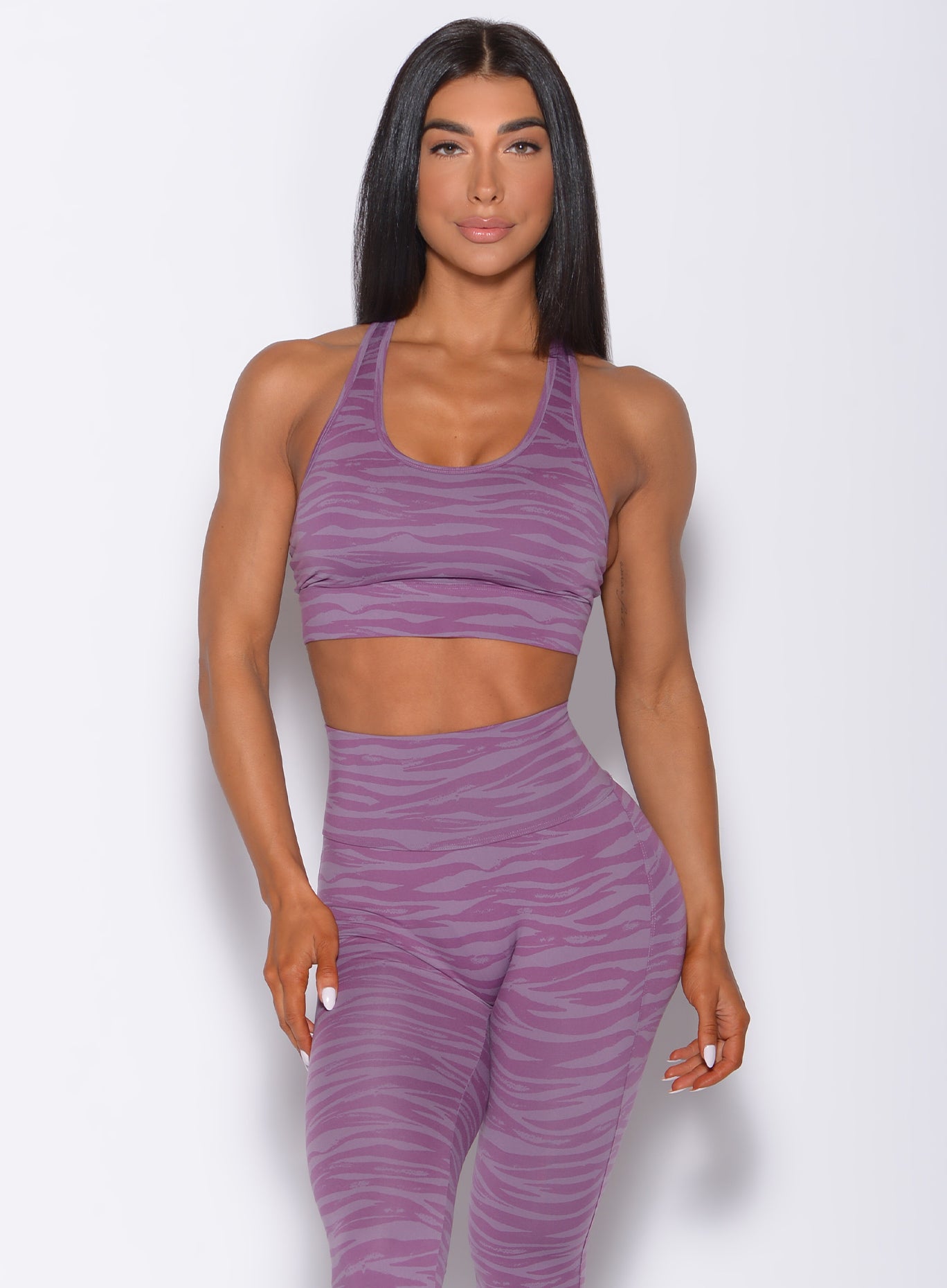 Front  profile view of a model in our tiger printed rival sports bra in orchid purple color and a matching sexy back leggings with criss cross straps at the back