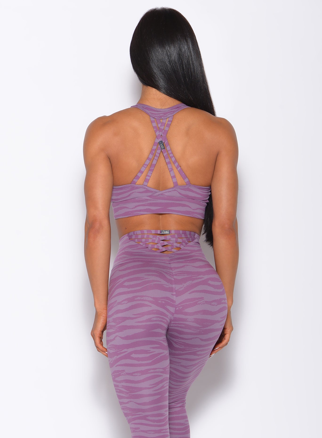 Back  profile view of a model wearing our tiger printed rival sports bra in orchid purple color and a matching sexy back leggings