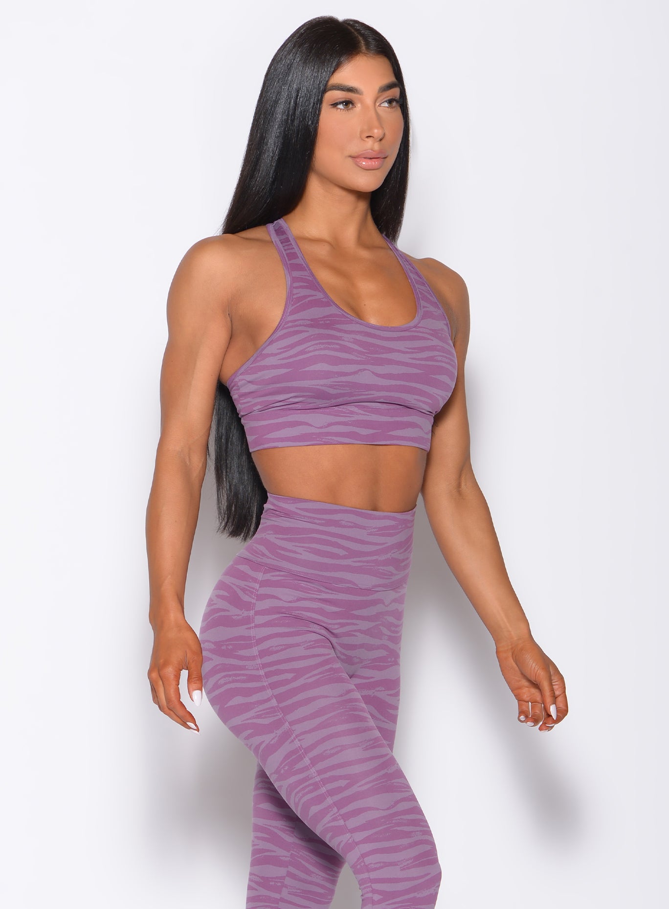 Right side  profile view of a model angled right wearing our tiger printed rival sports bra in orchid purple color and a matching sexy back leggings