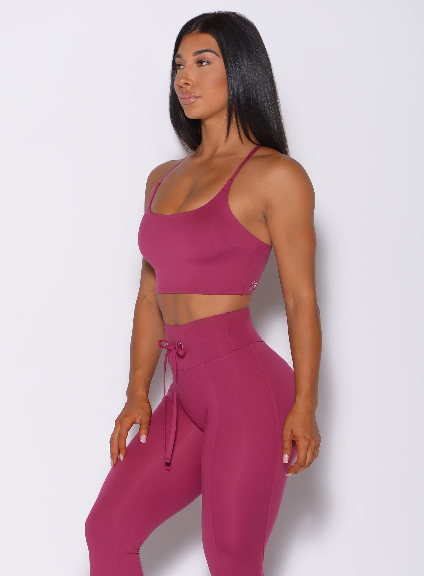 Left side profile view of a model facing forward wearing our cross fit sports bra in berry good color and a matching leggings