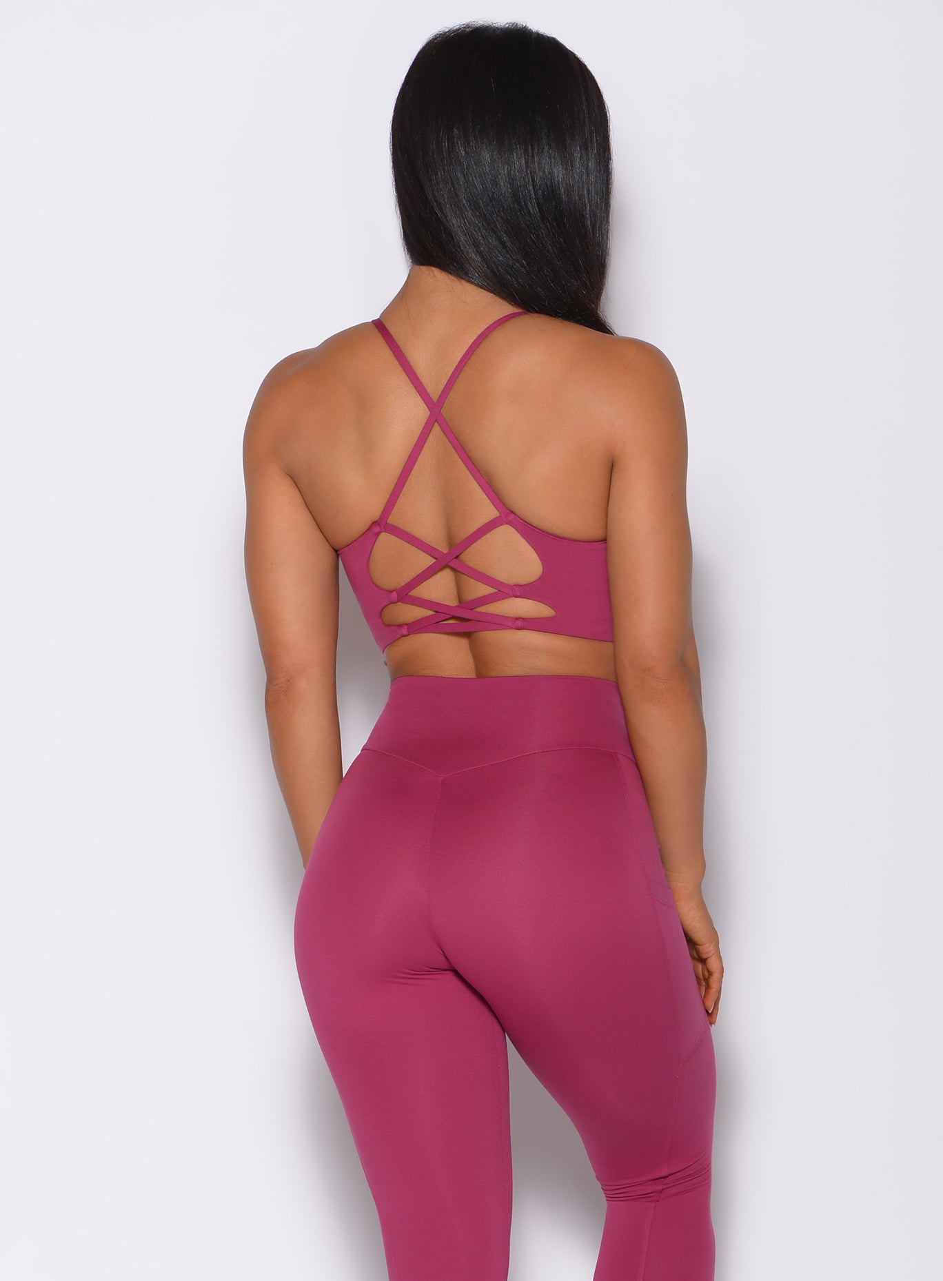 Back profile view of a model in our cross fit sports bra in berry good color and a matching leggings 