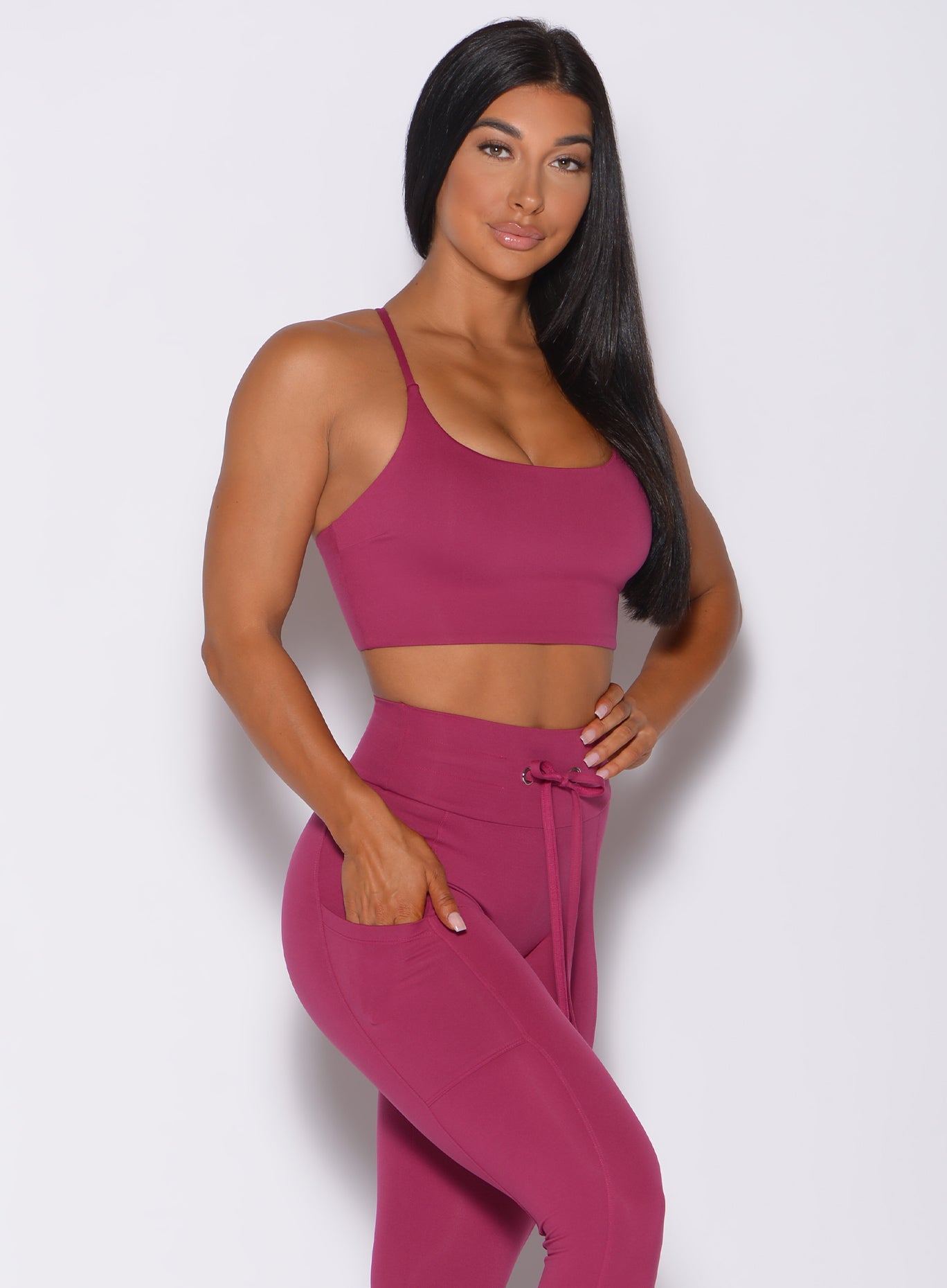 Right side profile view of a model angled right wearing our cross fit sports bra in berry good color and a matching leggings