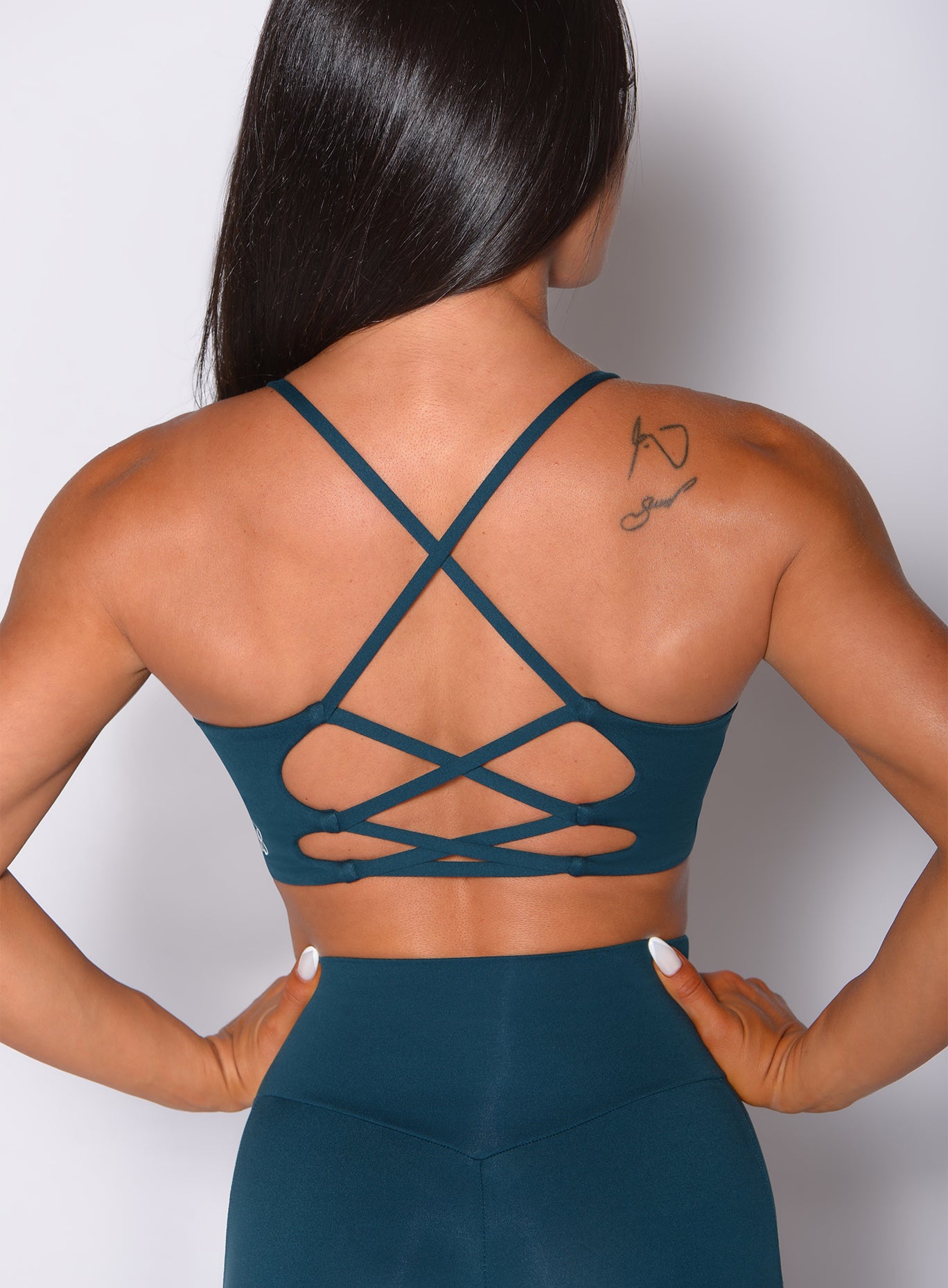 Zoomed in back profile view of a model in our cross fit sports bra in peacock color and a matching leggings