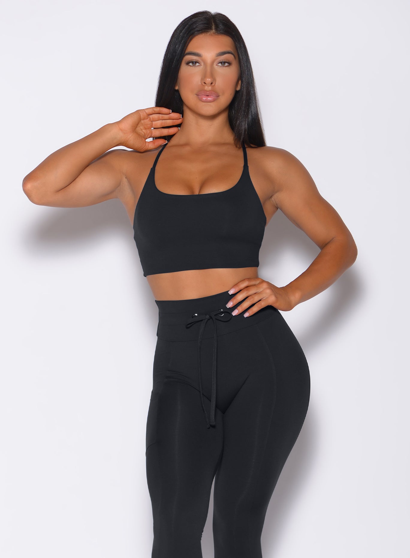 Front profile view of a model with her left hand on waist wearing our black Cross Fit Sports Bra and a matching black leggings