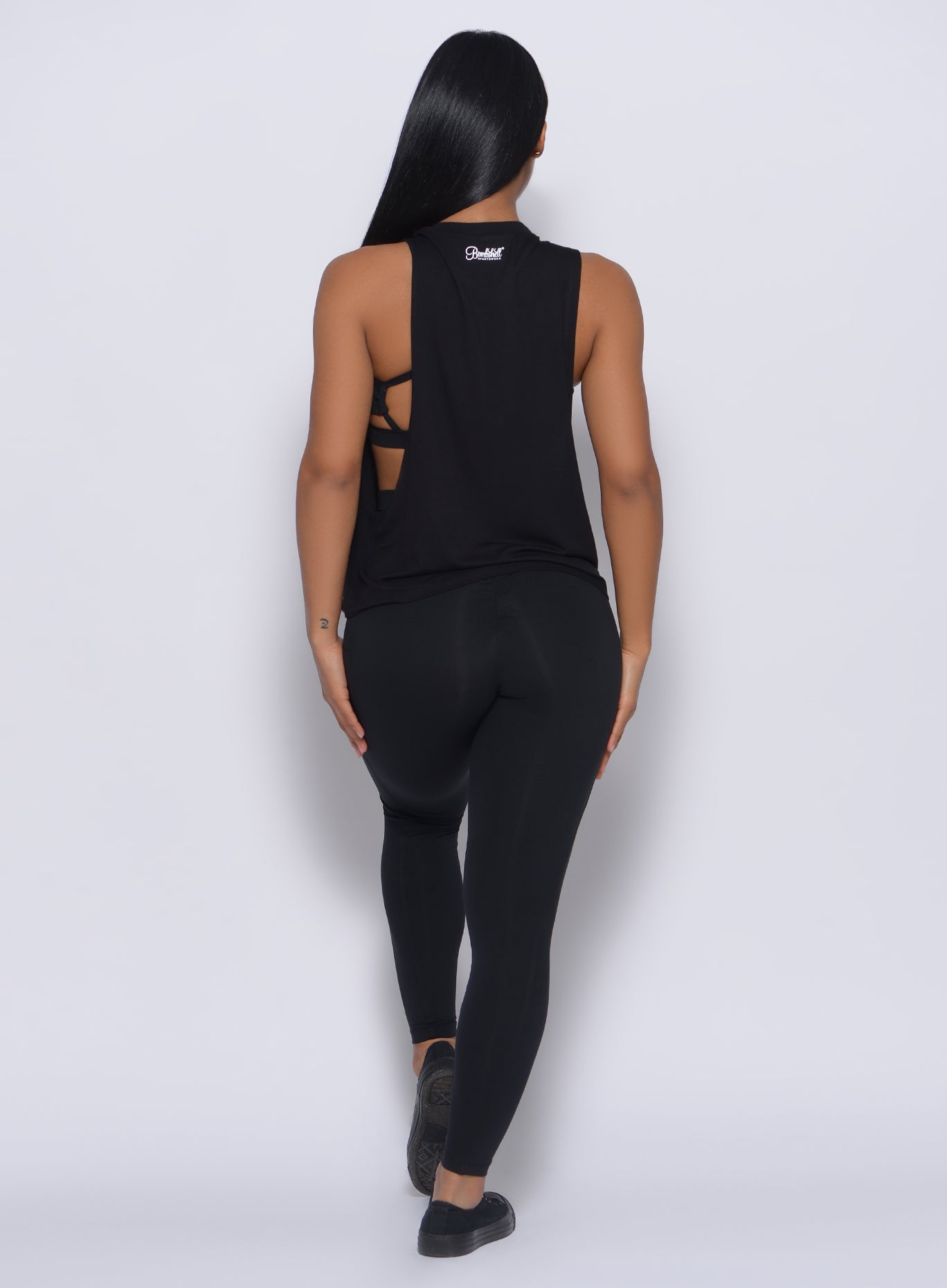 Back profile view of a model wearing our black muscle tank and a matching leggings