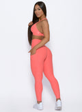 left side profile view of a model facing to her left wearing our Curve leggings and Braid Back Sports Bra in Coral color