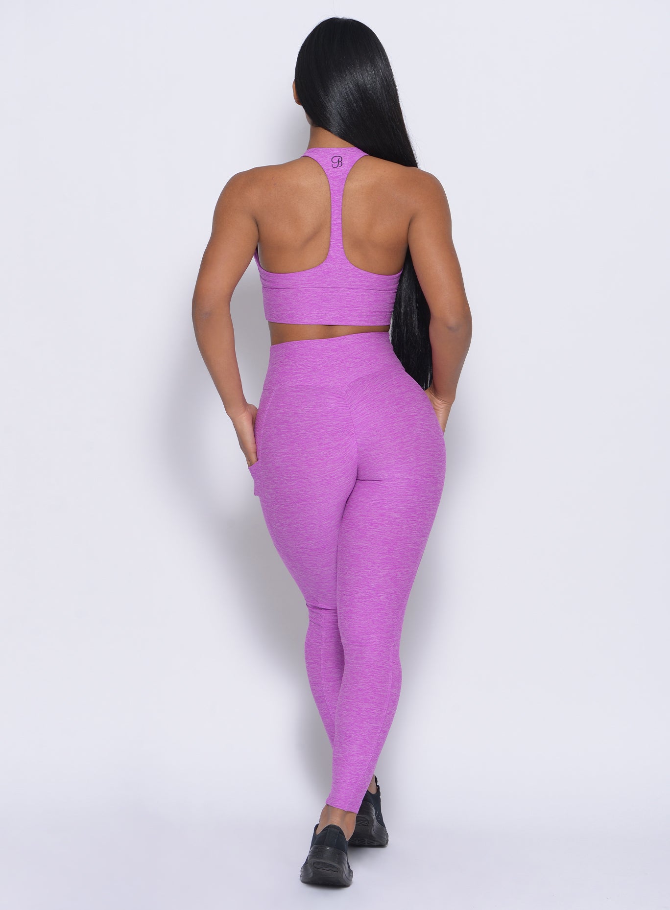 Back view of the model wearing our thrive leggings in purple color and a matching bra