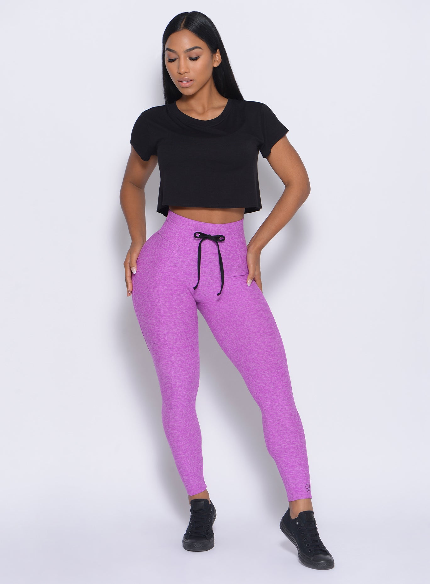 Front profile view of the model with her hands on  waist wearing our thrive leggings in purple and a black top