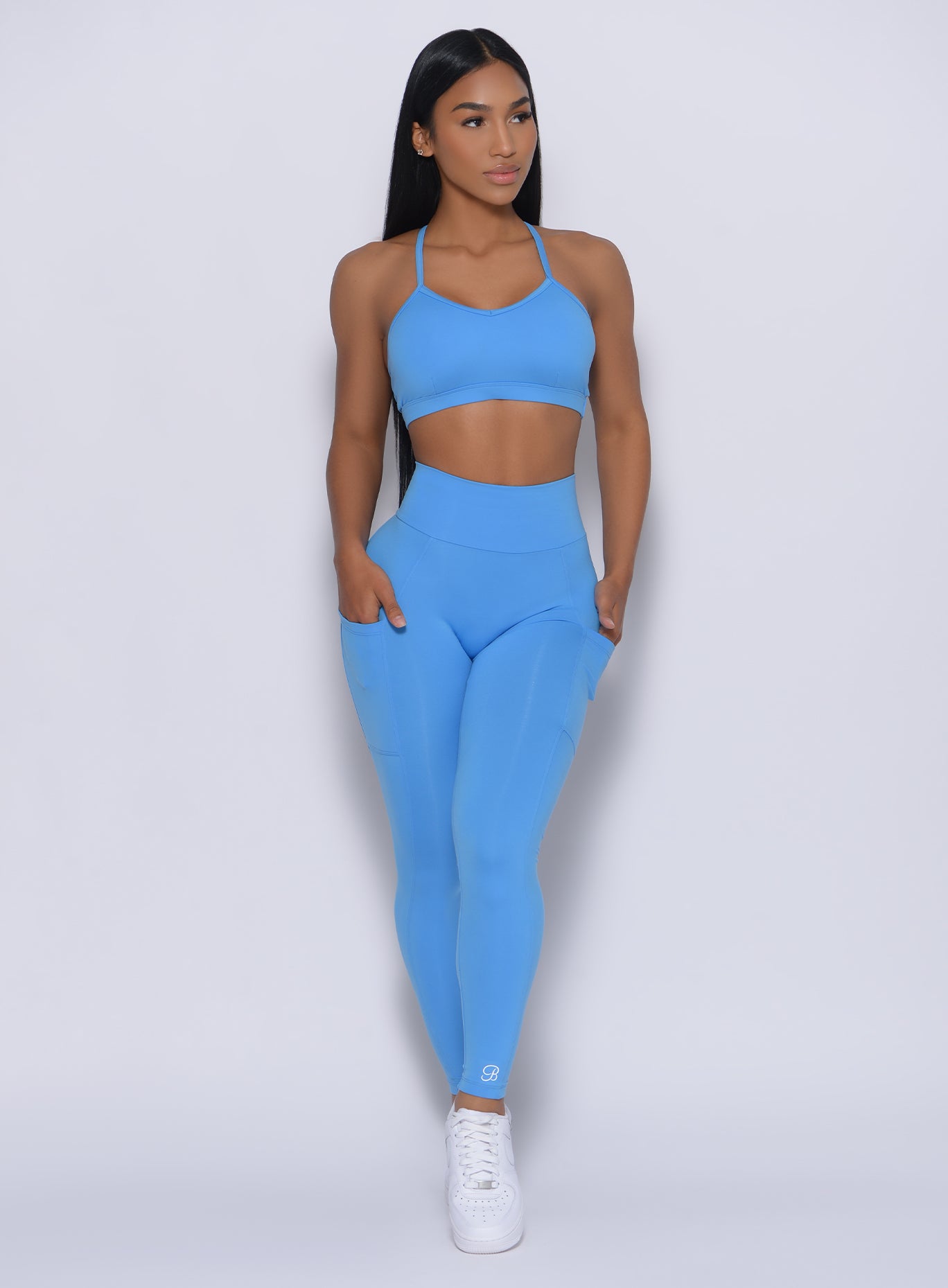 Front profile view of a model with her hands in pocket wearing our pumped sports bra in blazing blue color and a matching leggings 