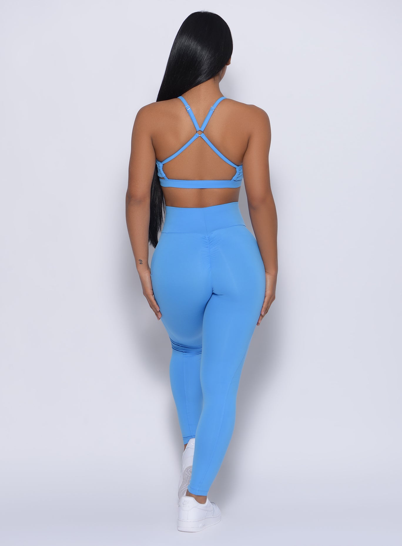 Back profile view of a model wearing our pumped sports bra in blazing blue color and a matching leggings